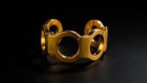 Bracelet menottes sculptural en or jaune posé sur un fond noir mat, éclairé par une lumière éditoriale contrastée dans une esthétique joaillerie parisienne des années 1970.
