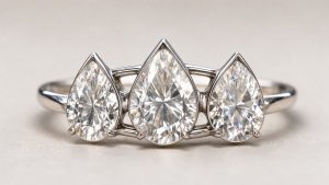Gros plan d’une bague de haute joaillerie en or blanc ornée de trois diamants taille poire semblant flotter, photographiée sur un fond neutre et élégant.